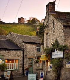 an old stone building with many windows and signs on the side of it in front of a grassy hill