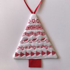 a red and white christmas tree ornament hanging from a red ribbon on a white wall