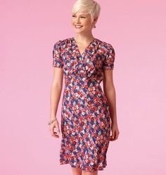 a woman standing in front of a pink background wearing a dress with flowers on it