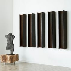 an abstract sculpture sits on a wooden table in front of four metal pieces hanging on the wall