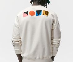 a man with dreadlocks standing in front of a white wall wearing a sweatshirt that says love