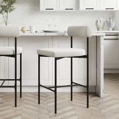 two white bar stools sitting in front of a kitchen counter