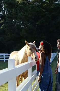 two people standing next to a white fence with a horse sticking its head over the fence