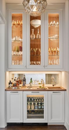 a kitchen with white cabinets and glass shelves filled with wine bottles, glasses, and other condiments