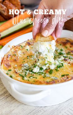 a hand dipping a piece of bread into a casserole dish with cheese and herbs