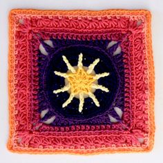 a crocheted square with an orange and purple star in the center, on a white surface