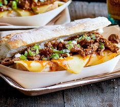 a sandwich with meat, cheese and green onions in a bowl on a wooden table