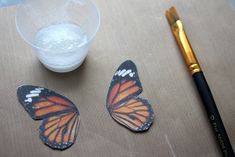 two butterflies sitting on top of a table next to a paintbrush and a bowl