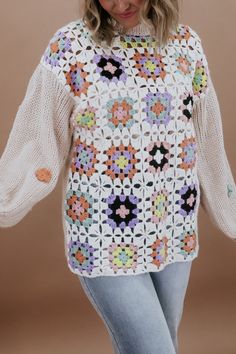 a woman wearing a white crochet sweater with colorful flowers on the shoulders and sleeves