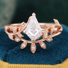 a rose gold ring with a white diamond in the center and leaves around it on a blue velvet cushion