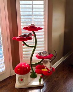 a cat tree with red flowers and two mice on it's base in front of a window