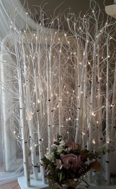 a vase filled with flowers sitting on top of a table next to white trees covered in lights