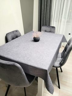 a dining room table with grey chairs and a vase on the top, in front of a window