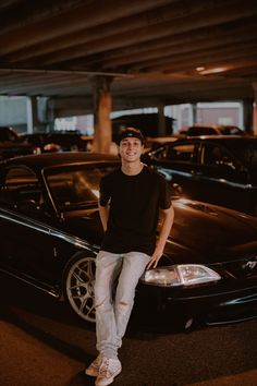 a man sitting on the hood of a car in a parking garage with other cars