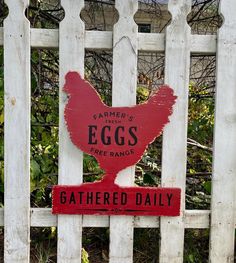 a red sign on a white fence that says, farmer's eggs free range gathered daily