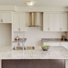 a kitchen with white cabinets and marble counter tops