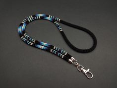 a blue and black lanyard with silver hardware on a gray background, the lanyard has a metal hook attached to it