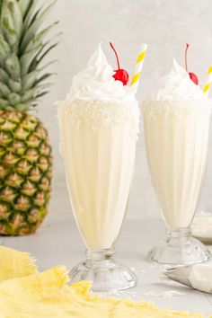 two glasses filled with milkshakes next to a pineapple