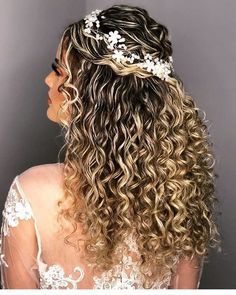 the back of a woman's head with long curly hair and flowers in her hair