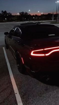 a black dodge charger parked in a parking lot at night with its lights on