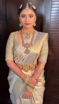 a woman in a white and gold sari with her hands on her hips, wearing jewelry