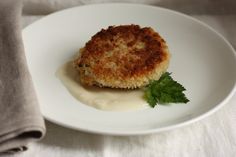 a piece of crab cake on a plate with sauce and parsley garnish