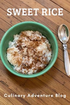 a green bowl filled with food on top of a wooden table next to a spoon