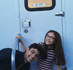 a man and woman posing for a photo in front of a door with the words kitty on it