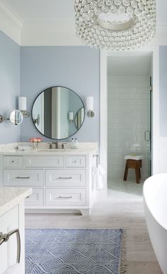 a white bath tub sitting next to a bathroom sink under a round mirror on a wall