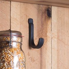 a mason jar filled with corn on top of a wooden shelf next to a hook