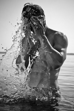 a shirtless man splashing water on his face