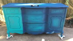 an old dresser painted in blue and green with wheels on the bottom, sitting outside next to a fence