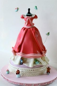 a cake that is shaped like a dress on top of a platter with little figurines around it