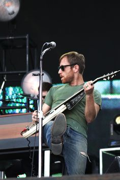 a man holding a guitar while standing next to a microphone on top of a stage