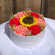 a flower arrangement in a round white box on a table with a wooden wall behind it