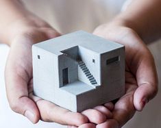 two hands holding a small model of a house with a spiral staircase coming out of it