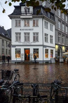 two bicycles parked in front of a white building on a cobblestone street with people walking by