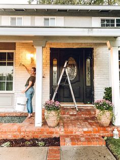 a woman standing on the front steps of a house with a bucket and ladder in her hand