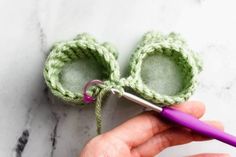 someone crocheting the ends of two baby booties with a purple knitting needle