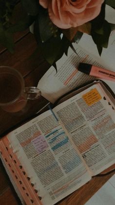 an open book sitting on top of a wooden table next to a vase with flowers