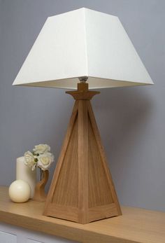 a wooden table lamp with a white shade on it next to a vase and candle