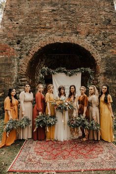 a group of women standing next to each other in front of a stone wall with greenery