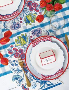 a table set with place settings for two people and red flowers on the table cloth