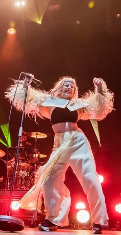 a woman in white pants and black top on stage