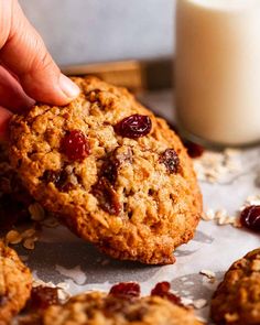 a person picking up some oatmeal cookies next to a glass of milk