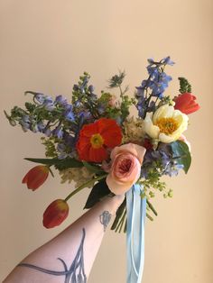 a woman's arm holding a bouquet of flowers and greenery in her left hand