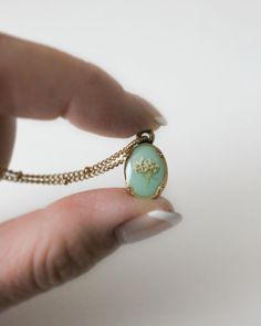 a woman's hand holding a dandelion pendant with a chain around it