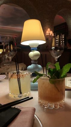 two cocktails are sitting on a table in a fancy restaurant with an old fashioned lamp