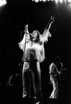 a woman standing on top of a stage with her arms in the air while holding a microphone