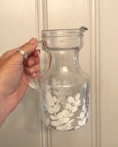 a hand holding a glass pitcher with white flowers on it